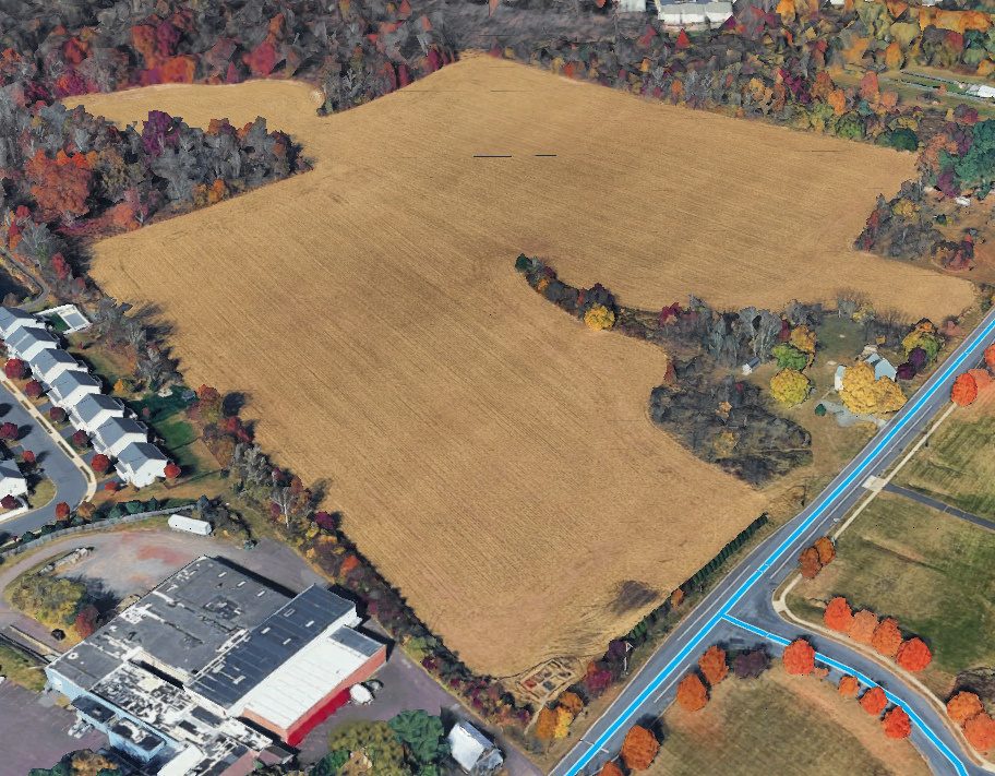An aerial view of the open farmland next to the site, bordered by autumn trees, houses and a road.